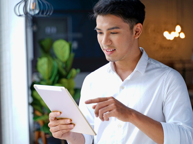 25 year old man in white shirt views real-time sales reports on his tablet with Hubbo POS.